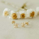 Gold flower-shaped earrings on a neutral background with dried flowers.