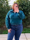 Person wearing a teal hoodie and blue jeans taking a mirror selfie outdoors.