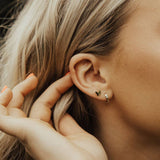 Close-up of an ear with a butterfly earring, hand adjusting hair.