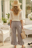 Woman in a white lace top and checkered pants standing in a sunroom.