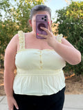 Person wearing a light yellow top outdoors with greenery in the background
