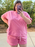 A woman taking a mirror selfie outdoors wearing a pink short-sleeve striped lounge set consisting of a t-shirt and matching shorts.