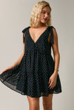 Woman wearing a black polka dot dress against a plain background