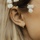 Close-up of an ear with a diamond earring and floral hair accessories.