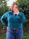 Person wearing a teal hoodie and blue jeans taking a mirror selfie outdoors.