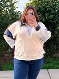 Person wearing a cream-colored sweatshirt with blue and gray accents outdoors.