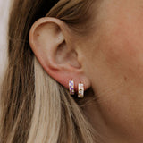 Close-up of an ear wearing colorful hoop earrings with blonde hair.