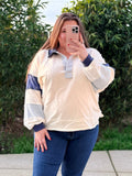 Person wearing a cream-colored pullover with blue accents outdoors.
