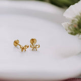 Gold bow-shaped earrings on a white surface with a blurred floral background