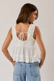 Woman wearing a white sleeveless top with ruffled details and blue jeans on a plain background