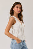 Woman wearing a white sleeveless top with lace details on a plain background