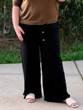Person wearing a brown top and black wide-leg pants standing on a concrete surface with grass in the background.
