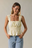 Woman wearing a light yellow sleeveless top and blue jeans against a neutral background