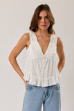 Woman wearing a white sleeveless top with ruffled details and blue jeans on a plain background