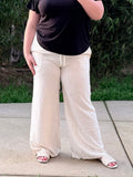 Person wearing a black top and white pants standing on a concrete surface with greenery in the background