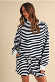 A woman wearing a matching navy and white striped lounge set, featuring a long-sleeve mock-neck sweatshirt and coordinating shorts, posed against a solid beige background.