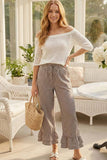 Woman in white off-shoulder top and checkered pants standing in a sunroom.