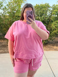 A woman taking a mirror selfie outdoors wearing a matching pink and white striped short-sleeve t-shirt and shorts set.
