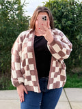 Person wearing a checkered cardigan outdoors with greenery in the background