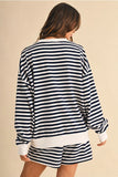 A woman shown from the back wearing a navy and white horizontally striped long-sleeve sweatshirt and matching shorts against a plain beige studio background.
