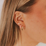 Close-up of an ear wearing gold hoop earrings with a small heart-shaped earring.