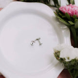 Silver earrings on a white surface with flowers in the background