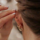 Close-up of a person wearing gold earrings with a blurred background